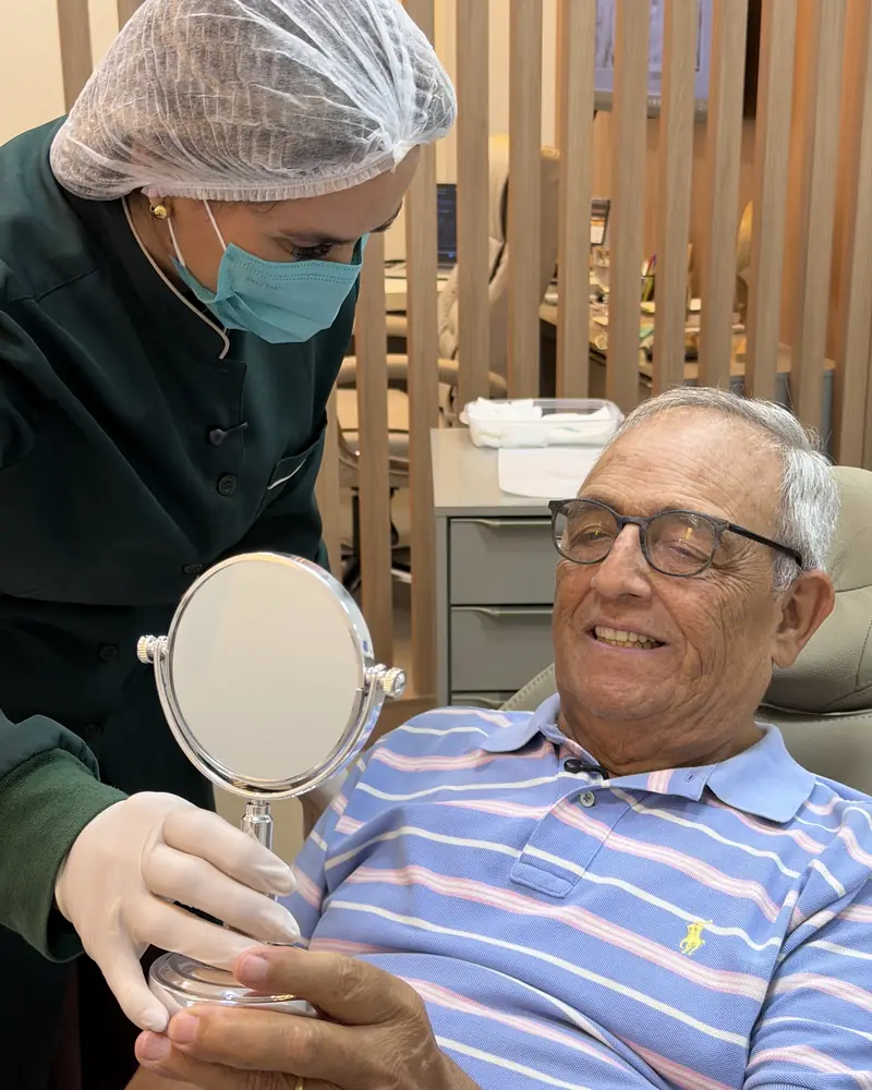 Paciente da Oral Sin Londrina sorrindo no espelho durante o atendimento